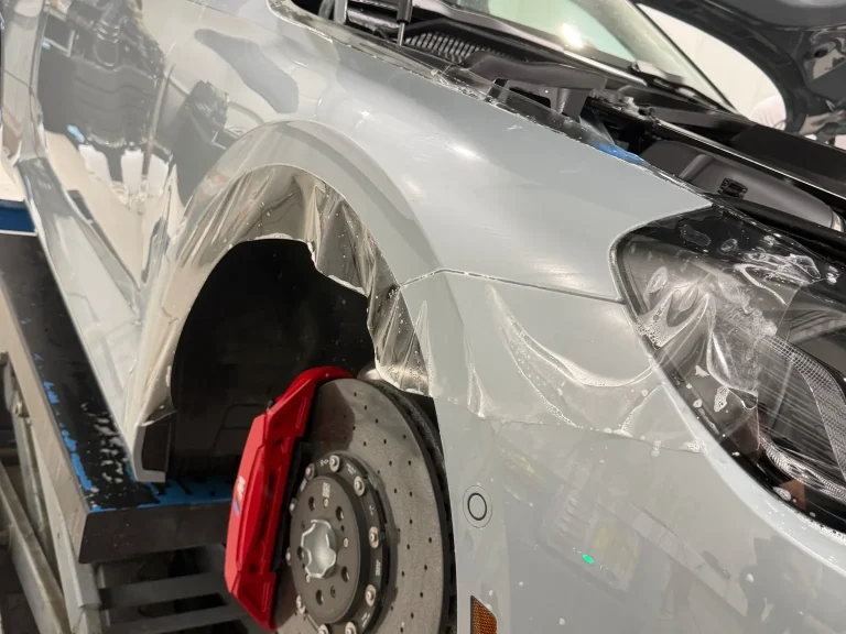 BMW M2 CS in Hellgrau, Montage der Lackschutzfolie an Kotflügel und Front in der Werkstatt